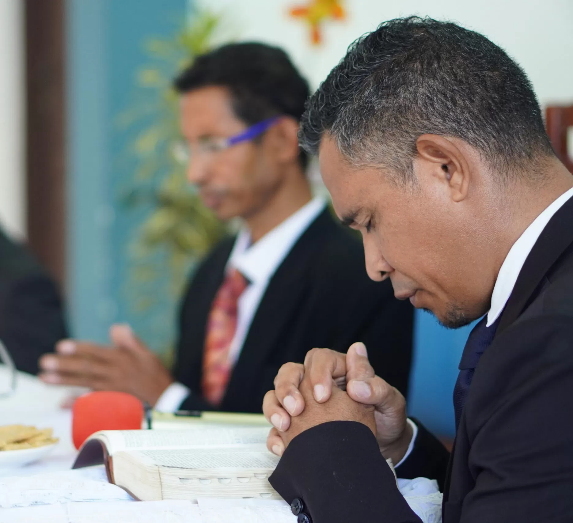 Two church members bow their heads in prayer over an open Bible